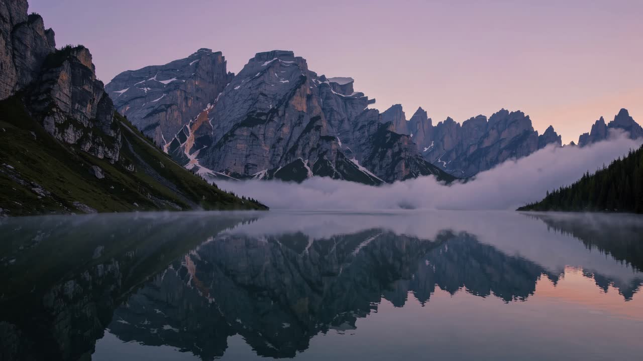 A serene mountain landscape at dawn, reflected in a calm lake. Captured from a low angle, this video