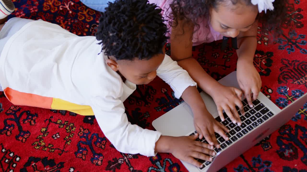 High angle view of cute black siblings using laptop in living room at comfortable home 4k