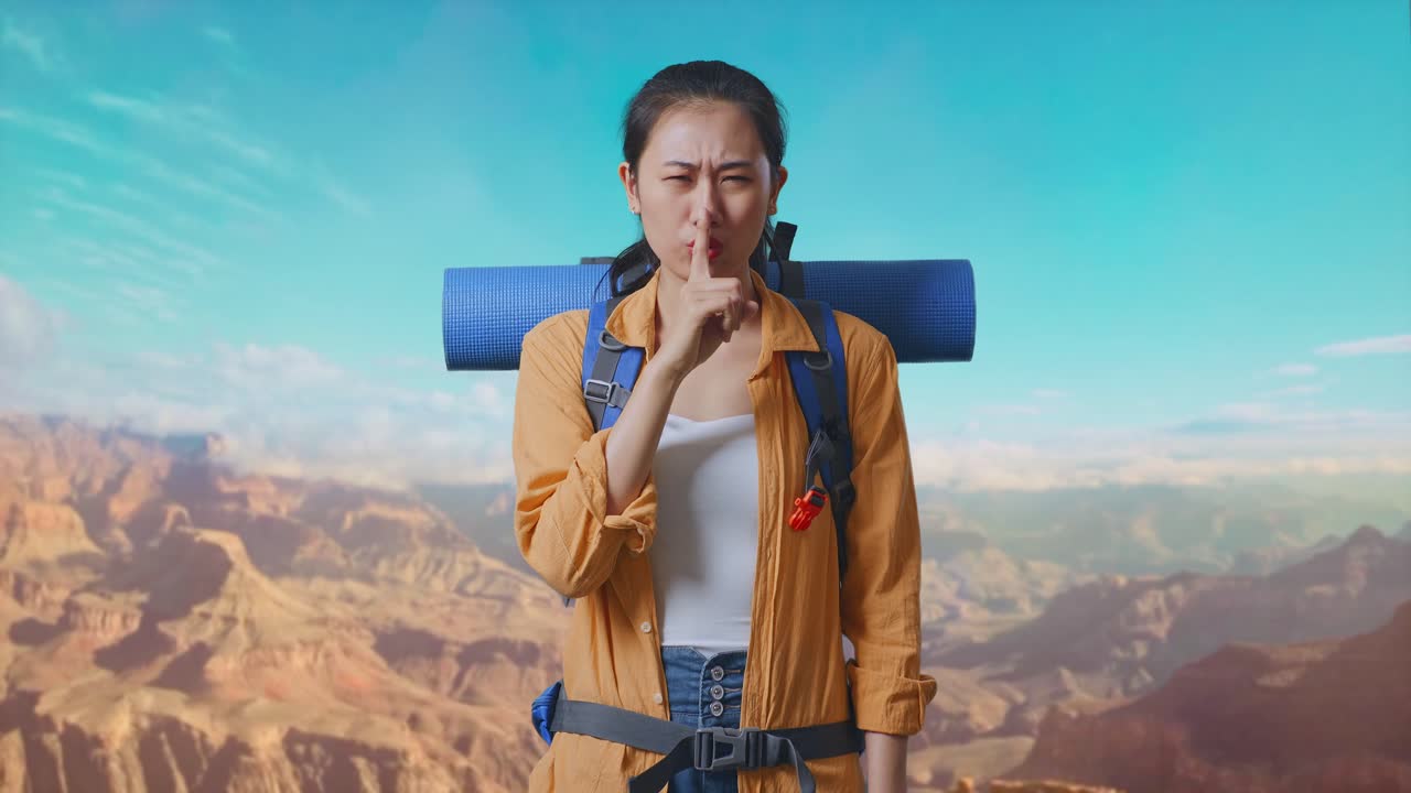 Asian Female Hiker With Mountaineering Backpack Looking At Camera And Making Shh Gesture While Traveling At The Top Of Mountain