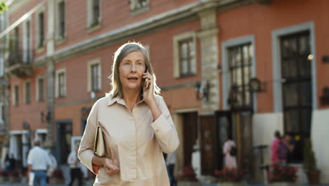 Señora-Mayor-Guapa-Caminando-Por-La-Calle-En-La-Ciudad-Vieja-Y-Hablando-Por-Teléfono-Inteligente