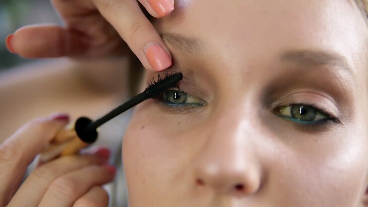 Close up of a make up process, model's eyes. Artist putting on black mascara. Front view