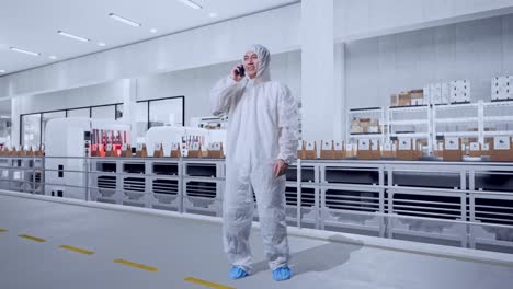 full body of asian male scientist talking on smartphone while standing with conveyor for packaging coffee beans in bags at coffee factory