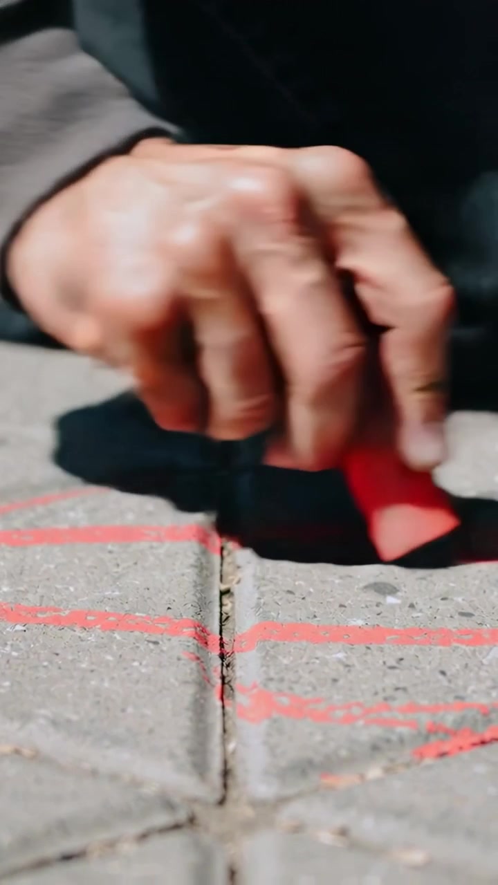 Vertical video: Moving sweatshirt-sleeve drawing red chalk lines on tiles marking grout, copy space