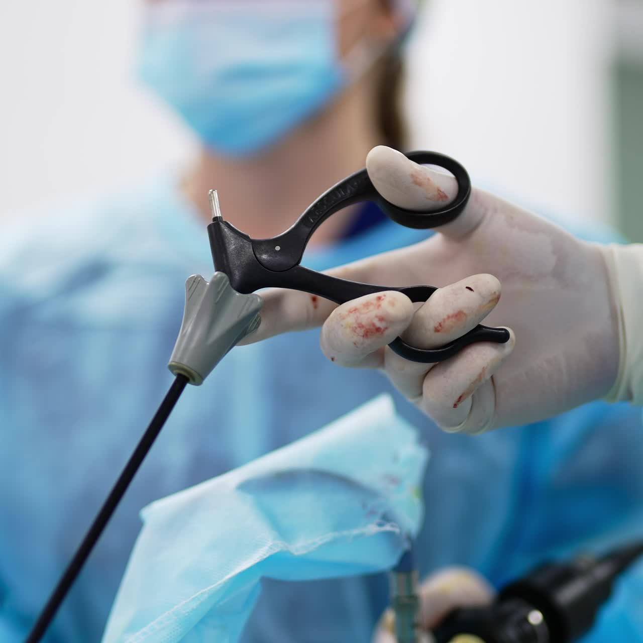 Surgeon's hands in latex gloves stained with blood holding instruments. Operation in process. Close up. Blurred background