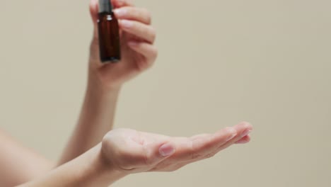 hands of woman holding flask with cosmetic on beige background with copy space, slow motion