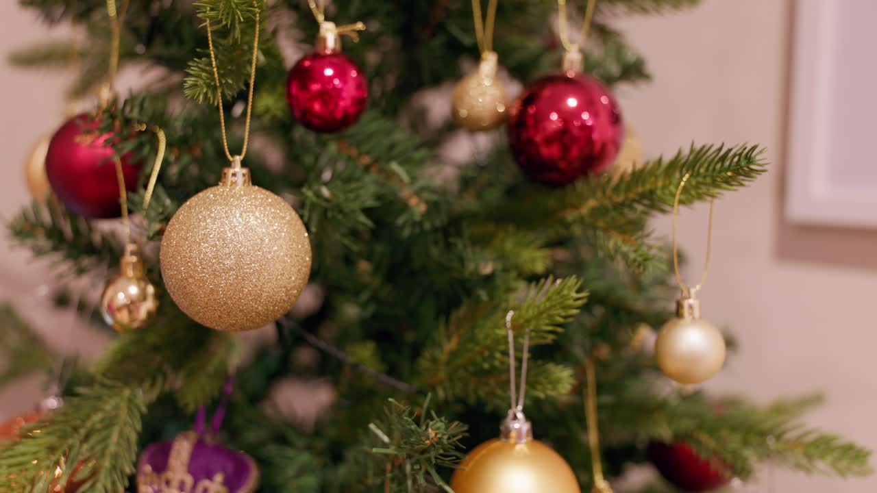 A festive close-up of red and gold baubles decorating a Christmas tree. The ornaments shine with elegance, even with the lights off, highlighting their texture and classic holiday charm.