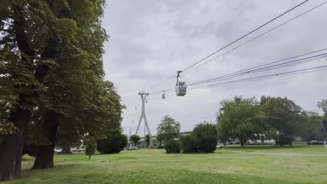 cable car station with gray pillars and small gondolas over a meadow with trees in cologne germany