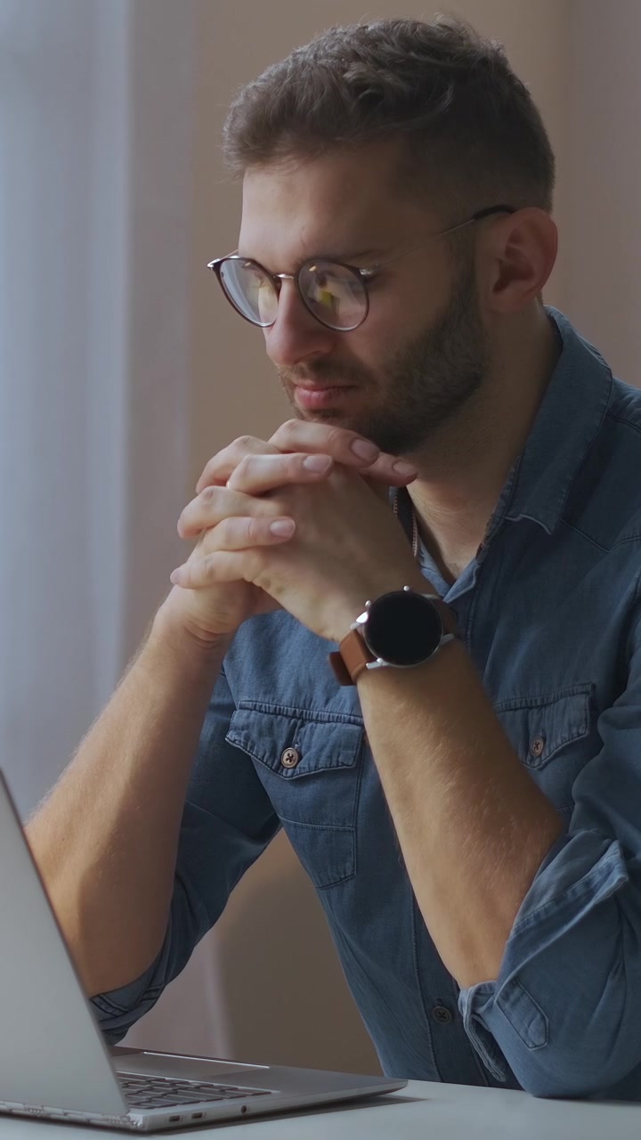 Giovane uomo pensieroso che lavora al portatile nell'ufficio di casa