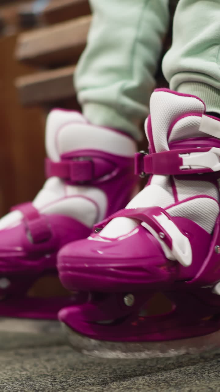 Close-up of a child's legs in pink and white ice skates with pink shoe close by, playfully dangling and moving above the ground