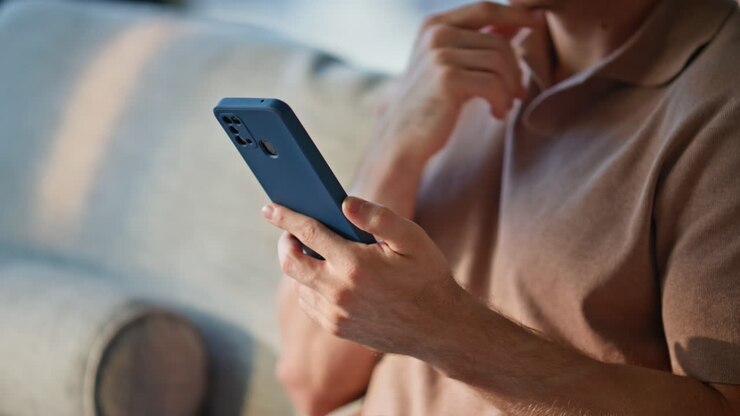 Primo piano di mani maschili che scorrono lo schermo di un cellulare scegliendo acquisti online a casa