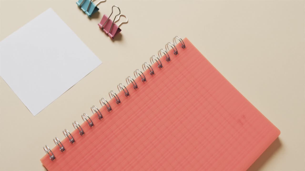 Close up of red notebook and school stationery arranged on beige background, in slow motion