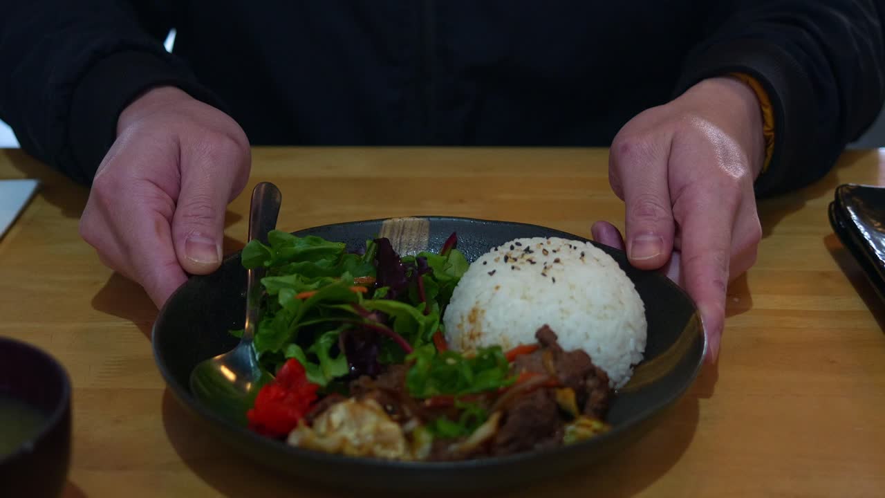 Hands holding a plate of rice, meat, and salad