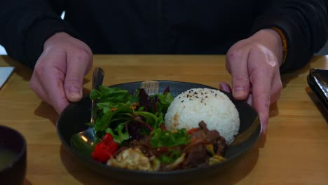 hands holding a plate of rice, meat, and salad