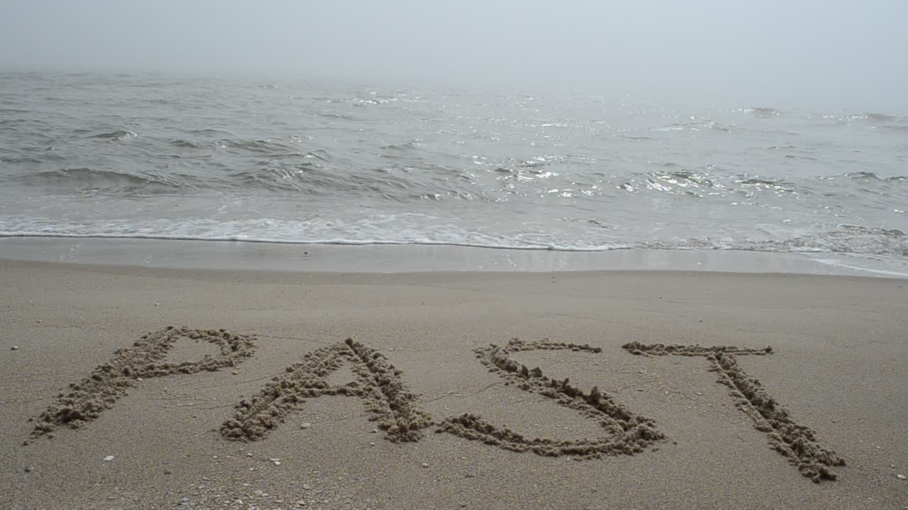 L'iscrizione "PAST" sulla sabbia bagnata della costa. Riprese in spiaggia.