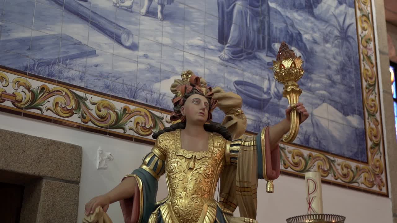 Primo piano di statua religiosa dorata con torcia all'interno di una chiesa.