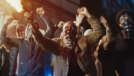 african american male rebel in hood and scarf on his face protesting at aggressive demonstration with molotov cocktail