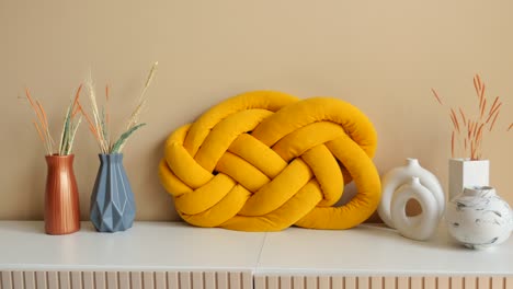 almohada de nudo amarillo y jarrones en un estante