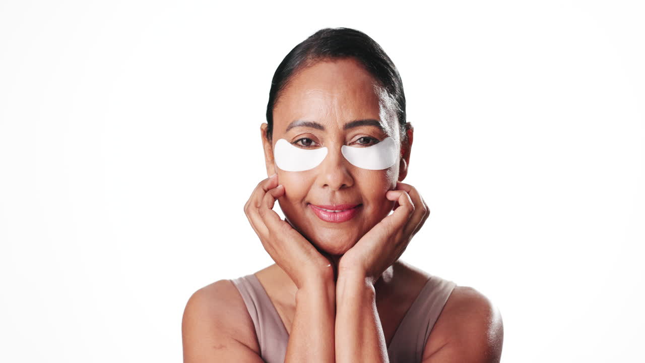 Mature Woman Smiling with Under Eye Patches on White Background