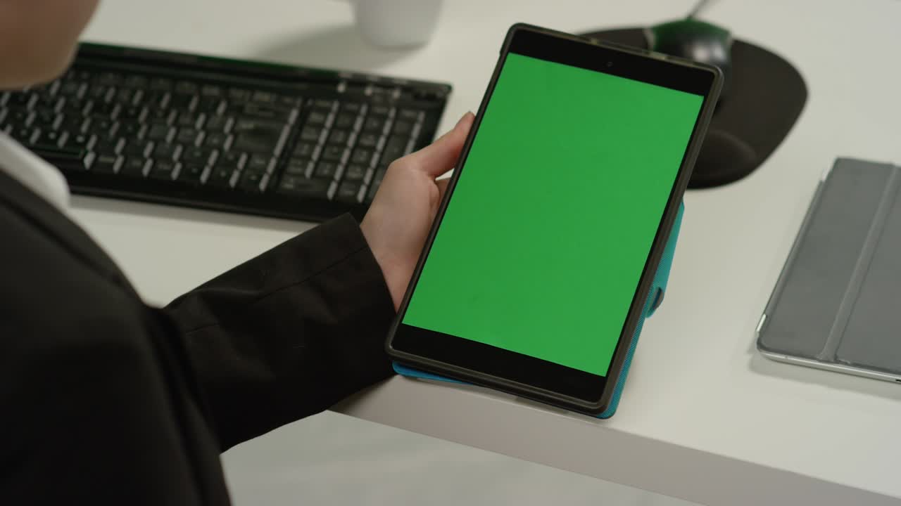 책상에 있는 cu 여성은 녹색 화면이 있는 태블릿을 보유하고 있습니다.