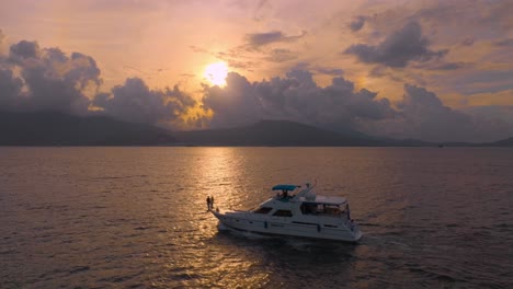 a breathtaking shot captures a yacht gracefully cruising across the ocean, bathed in the golden hues of a stunning sunset.