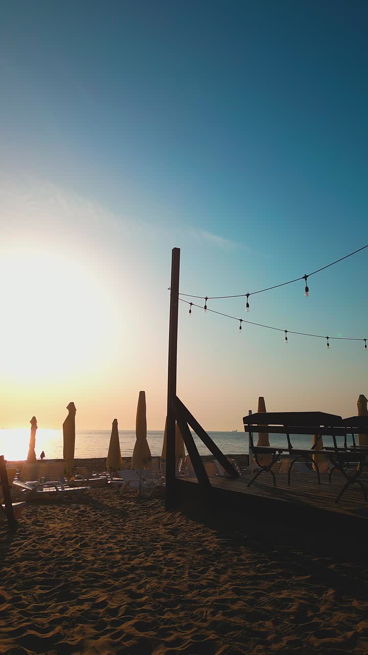 Silhouetted deck chairs and parasols in morning sun on sandy beach