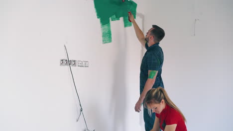 man paints room white wall with green young woman watches