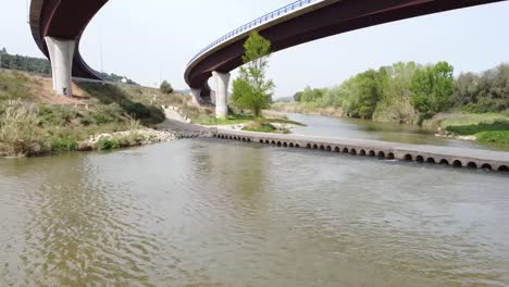 Bajo-Vuelo-Aéreo-A-Lo-Largo-Del-Río-Llobregat-Debajo-De-La-Carretera-De-Paso-Elevado-En-Cataluña