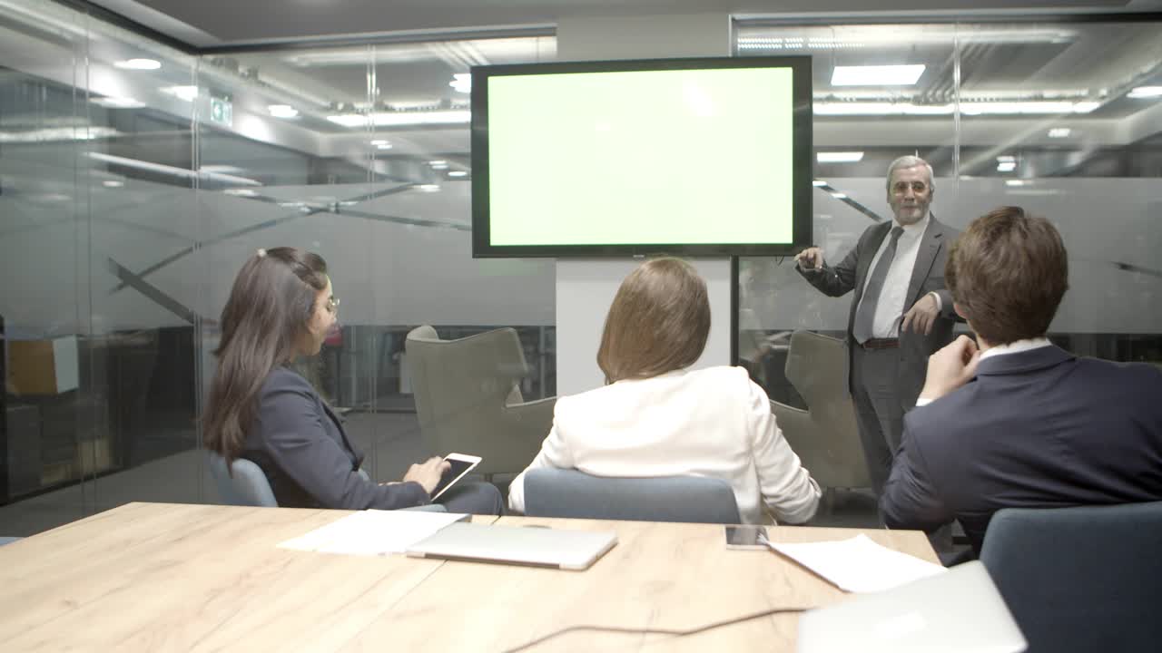 자신감 있는 성숙 한 연사 가 말 하고 디스플레이 를 가리키고 있다