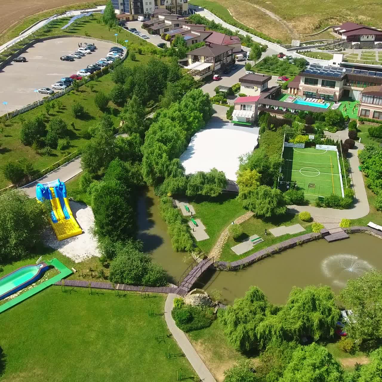 Recreational zone with private bungalows, swimming pools, tennis court and children playgrounds. People walking and resting in rural area. Top view