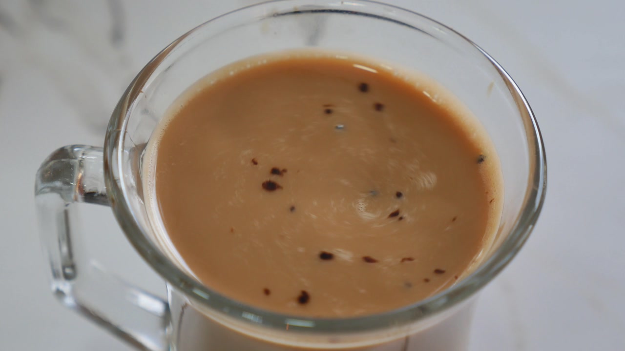 Close-up of a Hand Stirring Creamy Coffee in a Glass Mug