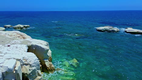 aerial drone forward moving shot over waves of ocean splashing on rocks along mediterranean sea waters in white rocks, cyprus on a sunny day