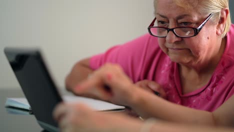 older woman with pink top and glasses looking at laptop in living room