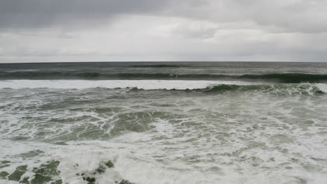 Beach-Front-View-Of-Ocean-Rough-Waves-and-Cloudy-Gray-Sky-At-Neskowin-Oregon-Coast,-backwards-aerial-shot