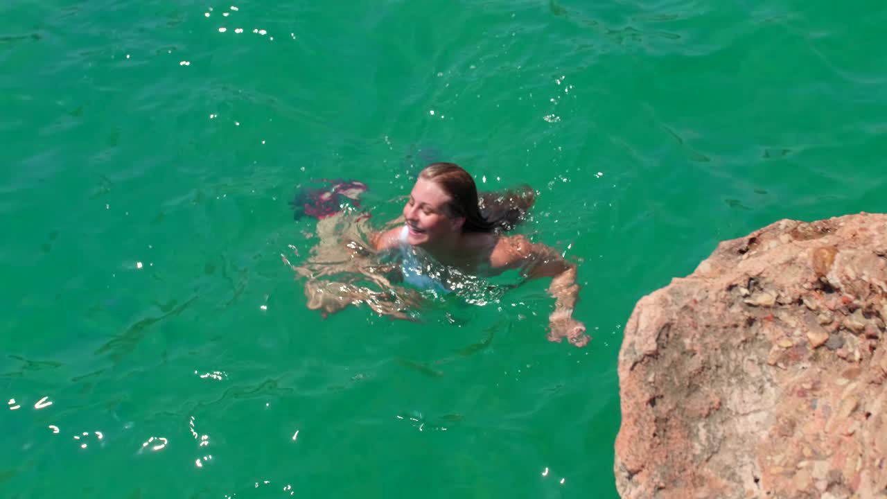 Ragazza bionda che nuota in acque limpide, blu e calme, facendo la rana e concentrandosi sull'acqua. È in vacanza nel sud della Spagna e si gode le ferie e la tranquillità che queste le portano