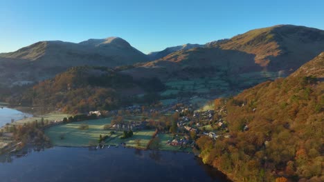 pueblo junto al lago rodeado de montañas al amanecer en otoño con vuelo lejos de la aldea