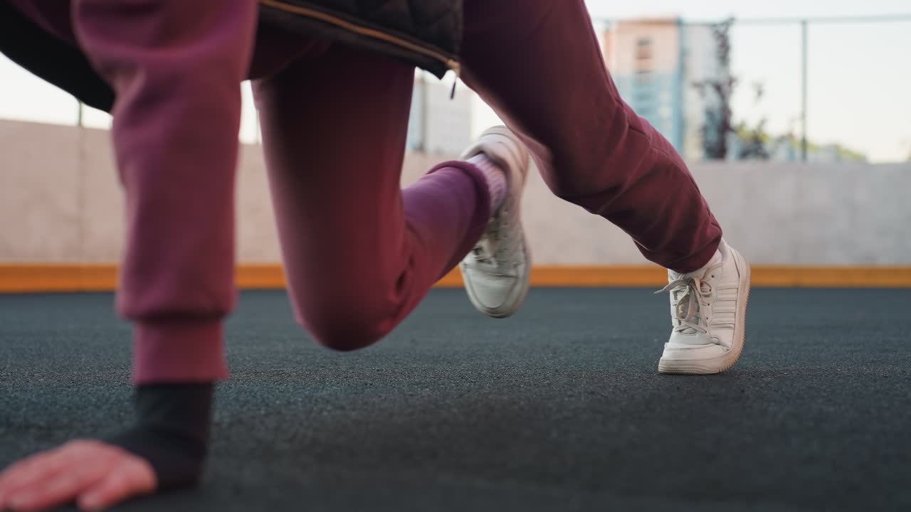 Leg view of female coach performing foot crawl exercise on urban sports court floor with hands pressing asphalt surface and legs moving for core stability and endurance in outdoor city workout routine
