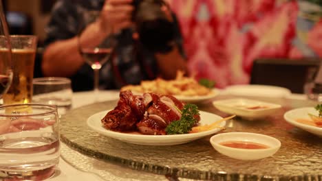 a rotating lazy susan in a restaurant displays chinese dishes and drinks, with a person photographing the scene