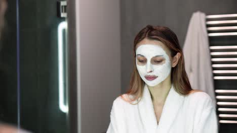 beautiful woman in bathrobe putting white mask for moisturizing using fingers, slowmo