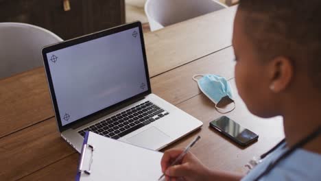 African-american-female-doctor-making-notes-during-video-call-using-laptop-with-copy-space