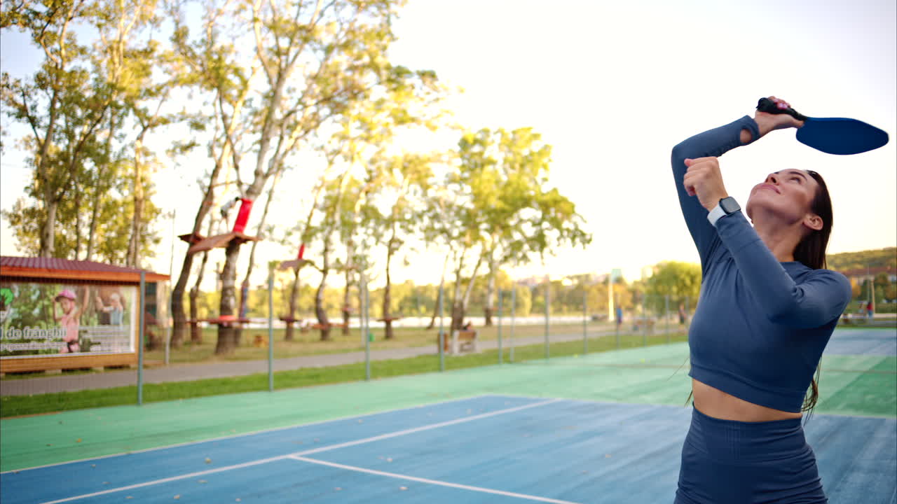 Women playing pickleball with yellow ball and blue paddle at a court