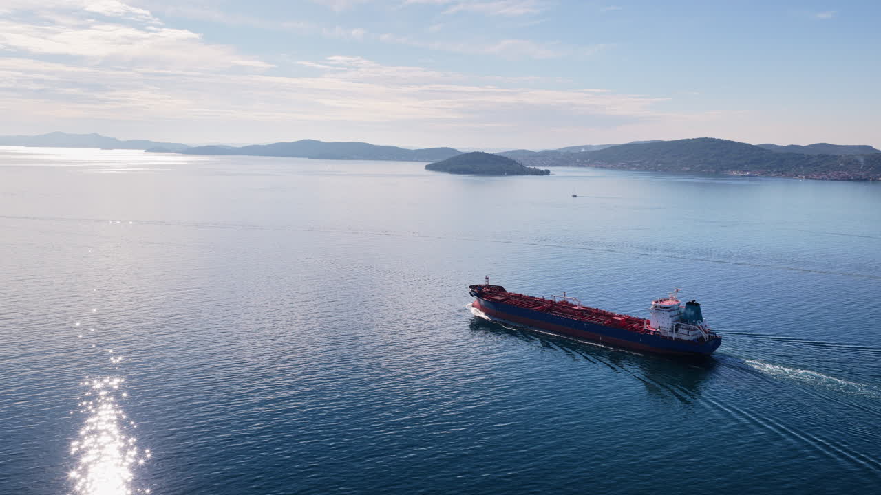 Aerial drone view of an oil tanker traveling across open Adriatic waters with distant mountain ridges and coastal towns visible on the horizon
