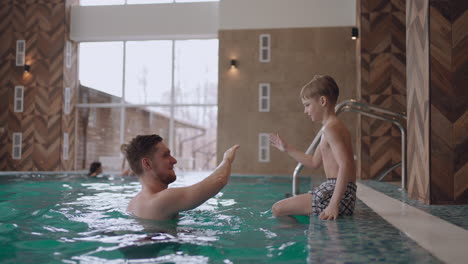 joyful little boy is playing with dad in swimming pool rest in family wellness center in weekend