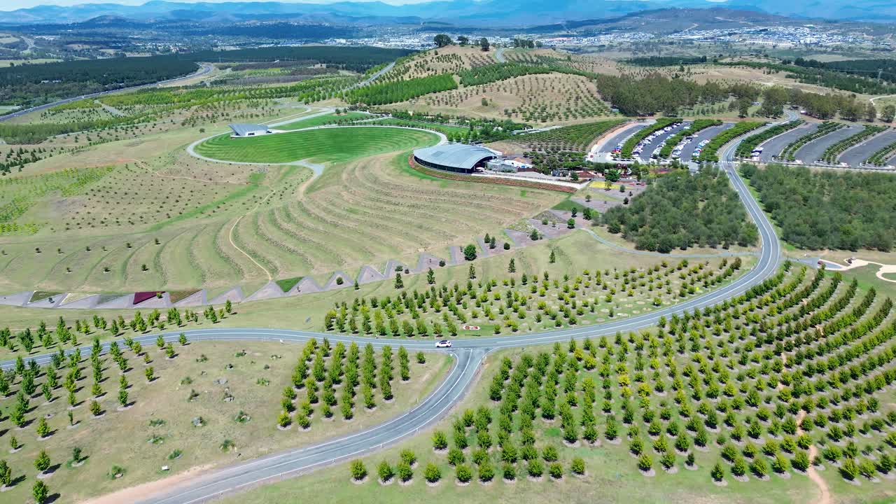 Drone aerial landscape of car vehicle driving winding road street at botanical gardens National Arboretum building in park grass valley Canberra ACT Australia travel tourism architecture rural