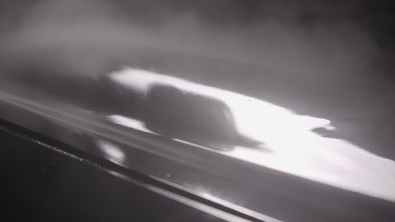 компрессорный распылятель наносит слои черной автокраски на кузов автомобиля