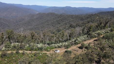 Aerial-Drone-shot-of-Four-Wheel-Drive-Toyota-driving-on-a-windy-road-with-mountains-in-the-background-near-Lake-Eildon,-Victoria-Australia