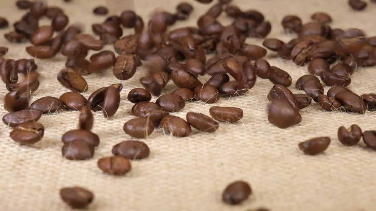 granos de café asados aroma arábica cayendo sobre fondo de yute