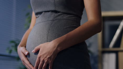 close up of pregnant businesswoman hands caressing her belly in the office