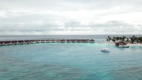 toma de drones de villas de agua, yates y una isla con palmeras en un resort de maldivas
