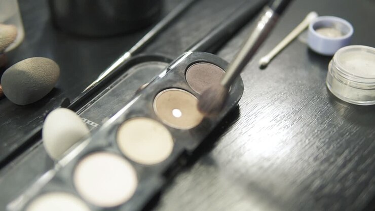 Focus moving from box with eyeshadows of different colours to the Close Up view of makeup artist applying eyeshadow on eyelid