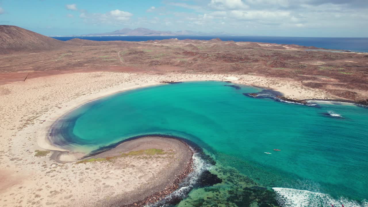4K aerial drone view of Playa de la Concha de Lobos, Fuerteventura, featuring turquoise waters, rocky coastlines, volcanic terrain, that showcase coastal beauty and serene landscapes